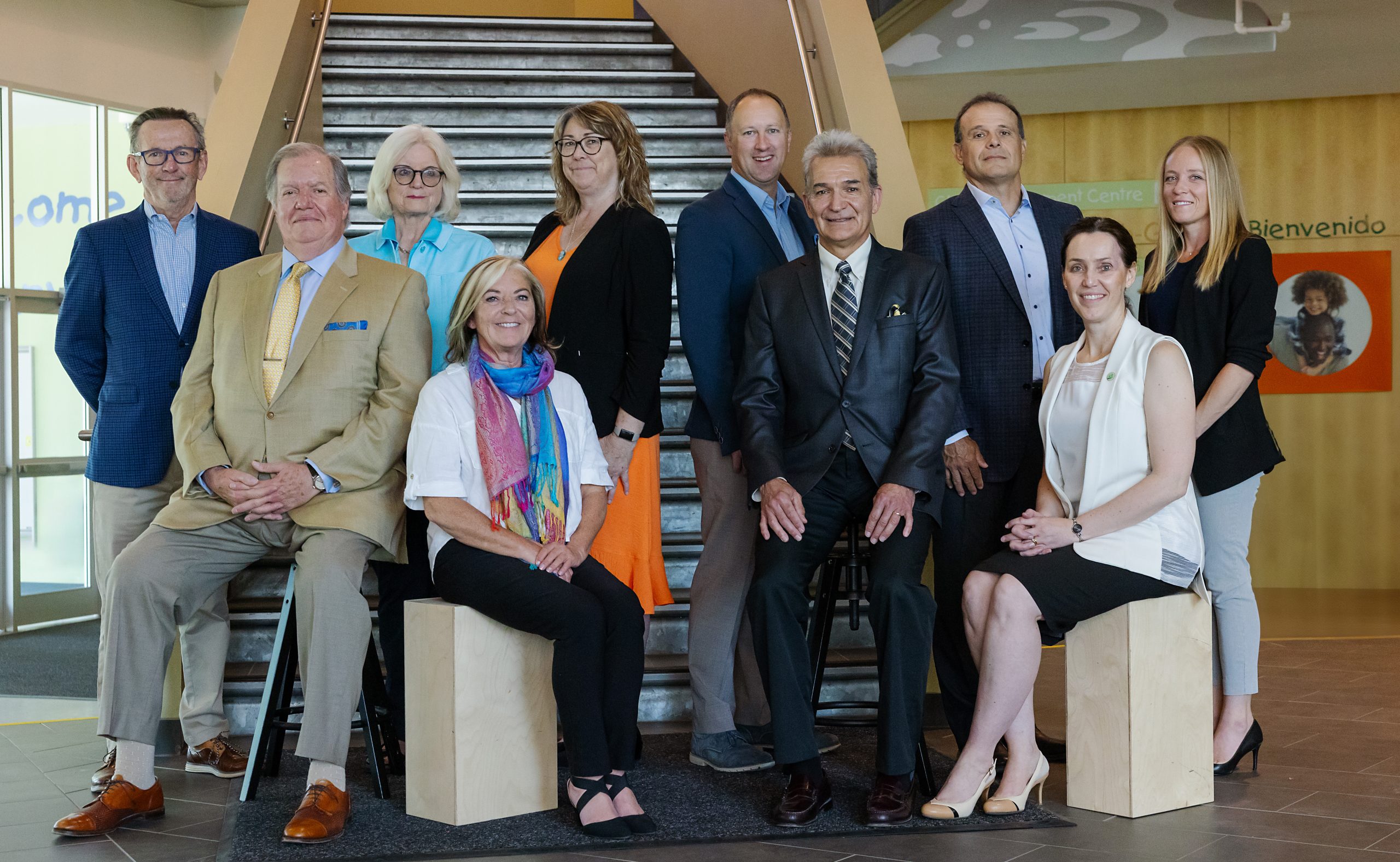 Group portrait of ten individuals in business or semi-casual attire, posed in two rows in front of a set of metal stairs. The individuals are the Board of Directors of The Sinneave Family Foundation.