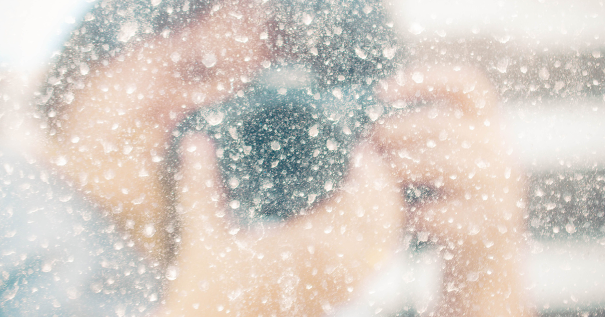 Shifting Perspectives image Blurred view of a person with a camera behind a water-splattered glass.